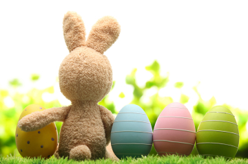 ein Stoffhase sitzt auf der Wiese, neben ihm sind bunte Ostereier